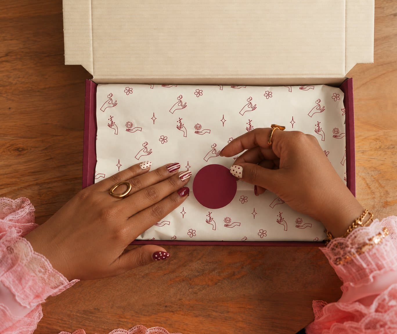 Hands sealing burgundy-patterned tissue paper inside a Sortout gift box